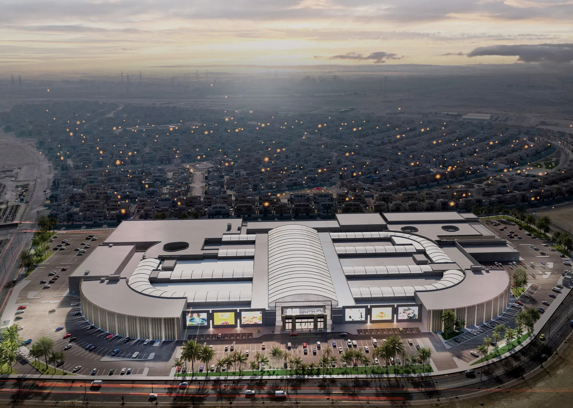 Aerial view of Ajyal Mall at dusk beside the road, with the residential district behind